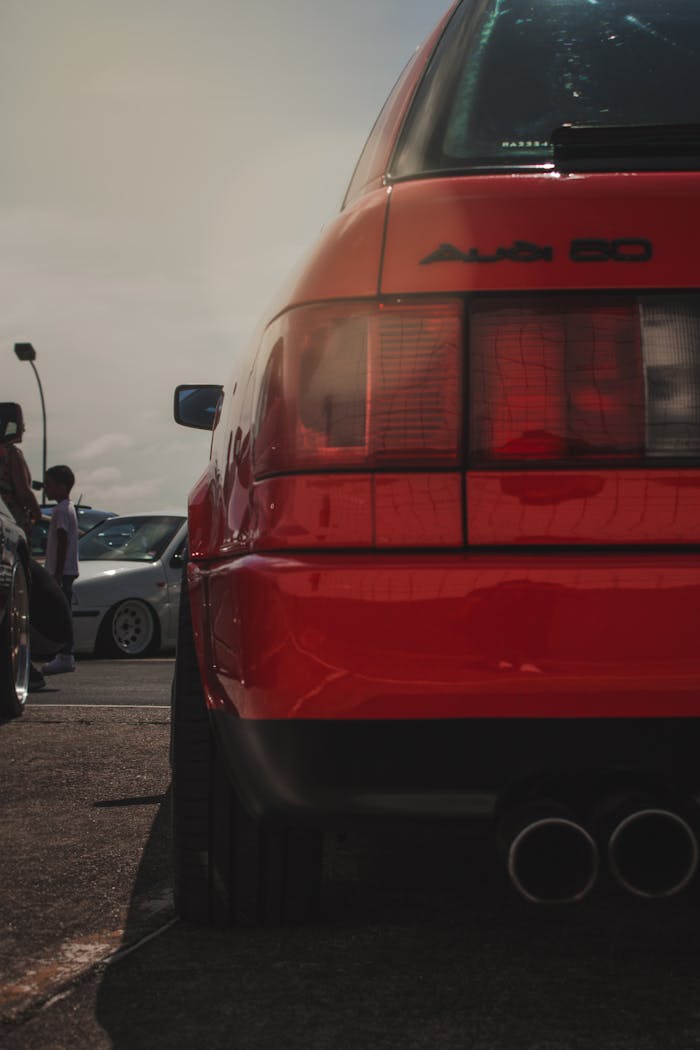 Rear view of red Audi 80 at an outdoor car exhibition with other vehicles.